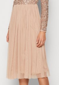 Top a maniche lunghe in perline con paillettes color oro rosa, abbinato a una gonna fluida e plissettata di lunghezza ginocchio in morbido tessuto beige trasparente.