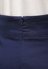Falda de tela de talle alto en color navy que presenta un zipper oculto en la parte posterior, textura suave y costuras limpias y ajustadas.