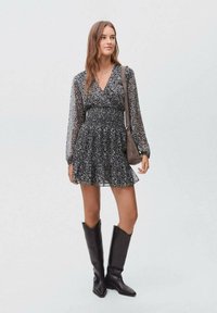 Černé šaty s potiskem, s nařaseným pasem, dlouhými průhlednými rukávy a rozevlátou sukní. Doplnené vysokými černými botami a kabelkou přes rameno.