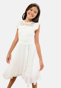 Biała sukienka z koronkowym gorsetem, falbaniastymi rękawami i zwiewnym asymetrycznym dołem. Posiada wiązany pasek w talii, co pozwala na regulację dopasowania.
