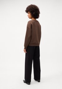 Brun crewneck sweatshirt kombineret med sorte vide bukser. Stoffet ser blødt ud med en afslappet pasform. Enkel design, ingen synlige mønstre eller accenter.