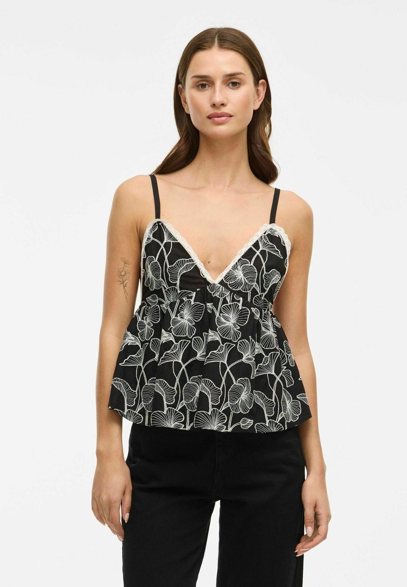 Camisole nera floreale con bordo in pizzo bianco, caratterizzata da una scollatura a V e spalline regolabili. Silhouette svasata con intricate fantasie floreali.