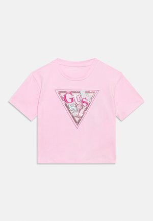 Lichtroze T-shirt met korte mouwen en een glanzende driehoekige logopatch met gemengde roze en zilveren letters die "GUESS" spellen.