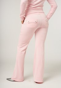 Roze flared broeken gemaakt van zacht materiaal, met twee achterzakken met drukknopen en een gladde, aansluitende tailleband.