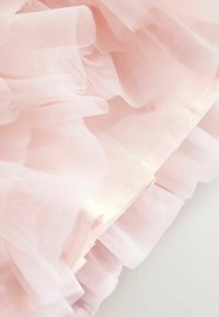 Měkká růžová průhledná tkanina vrstvená s volánkovou, plisovanou strukturou a jemným stehem podél okraje.