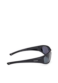 Gafas de sol polarizadas negras con un diseño elegante, que cuentan con un marco curvado y lentes oscuros. "Timberland" aparece en la patilla.