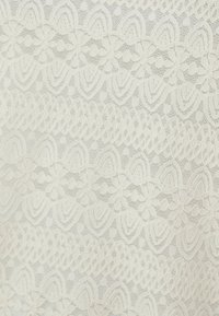 Tissu en dentelle de couleur blanc cassé avec des motifs floraux complexes et des bords festonnés. Présente une finition texturée délicate avec des éléments en relief.