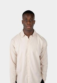 Lys beige langermet skjorte med knappelukking foran, med en klassisk krage og et strukturert stoff mot en nøytral bakgrunn.