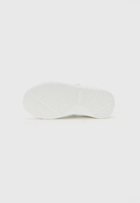 Semelle de chaussure blanche avec des rainures et des motifs de traction hexagonaux sur un fond blanc uni.