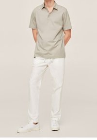 Polo košile světle šedé barvy z bavlny s límečkem na knoflíky, v kombinaci s bílými, lehkými kalhotami a bílými teniskami.