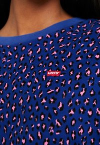 Blue shirt with pink and black leopard spots, featuring a small red Levi's logo tag near the neckline.