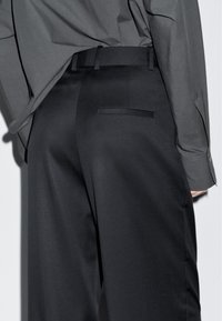 Czarne marynarskie spodnie o gładkiej fakturze, z tylną kieszenią i szlufkami na pasek, połączone z luźną, szaro button-up koszulą.