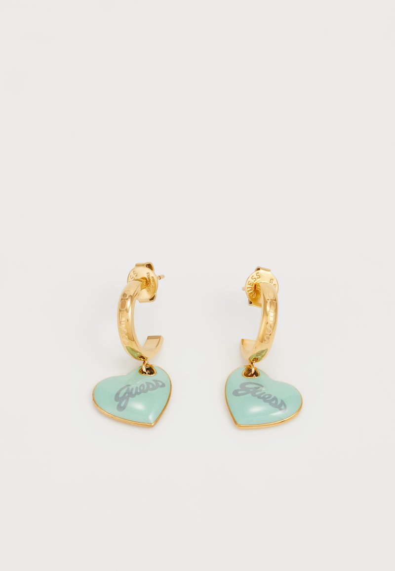 Pendientes de aro dorados con un corazón de turquesa y "Guess" impreso en gris. El corazón está unido por un pequeño anillo en la base de cada aro.