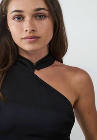 Top negro sin mangas con un escote asimétrico. Tejido suave, diseño ajustado y un pequeño detalle de cuello en un lado.