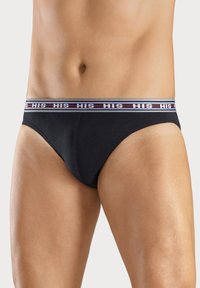 Schwarze Baumwollslips mit einem elastischen Bund in Weiß, Grau und Rot, der den Text "HIS" trägt. Glatte Textur, eng anliegende Passform.