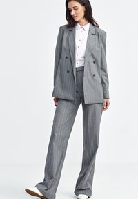 Szary garnitur w paski z podwójnym zapięciem i szerokimi spodniami, zestawiony z jasnoróżową koszulą z kołnierzykiem, z małymi guzikami.