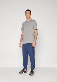 Gray short-sleeve t-shirt with a round neck, paired with navy blue tapered pants and black athletic shoes featuring red accents.