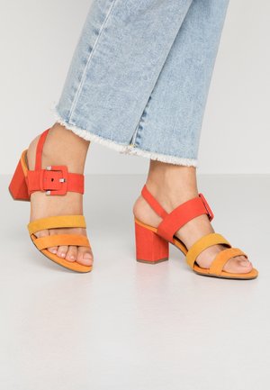 Farverige sandaletter med hæl, der har røde og gule ruskindsremme, en ankelrem med spædedetalje og en kraftig rød blokhæl.