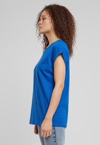 Mėlynas medvilninis trumpomis rankovėmis marškinėlis su apvalia iškirpte ir laisvo silueto, derinamas su šviesiai mėlynais džinsais. Paprastas dizainas, be matomų raštų.