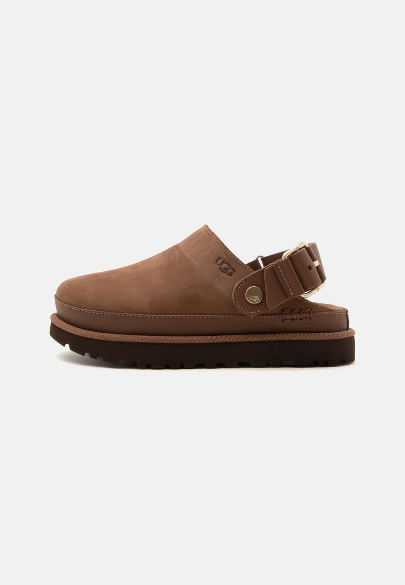 Sabot marron à enfiler avec une bride boucle ajustable, semelle noire épaisse et logo UGG sur le côté, présenté de profil sur fond blanc.