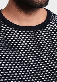 Pull en maille bleu marine avec motif dôme texturé blanc, col rond, et une finition douce, mettant en valeur un design structuré.