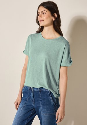 Lichtgroene T-shirt met korte mouwen, een ronde halslijn, een iets losse pasvorm en opgerolde mouwen, gecombineerd met blauwe jeans. Eenvoudige textuur.