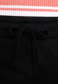 Svarta mjukisbyxor med en texturerad midja. Har en dragsko framtill och en kontrasterande detalj i korallrosa och vitt randigt vid toppen.