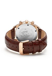 Montre avec bracelet en cuir brun imitation crocodile et boîtier en rose gold. Elle possède trois boutons-poussoirs et un dos en argent avec un design gravé.