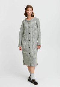 Vestido de cárdigan gris de punto que presenta patrones de trenzado, cierres de botones, mangas largas y aberturas en los laterales, elaborado con una suave mezcla de lana texturizada.