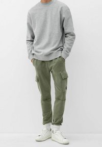 Grijze sweatshirt met geribbelde manchetten, gecombineerd met olijfgroene cargobroeken met zijzakken en taps toelopende benen. Witte sneakers maken de outfit af.