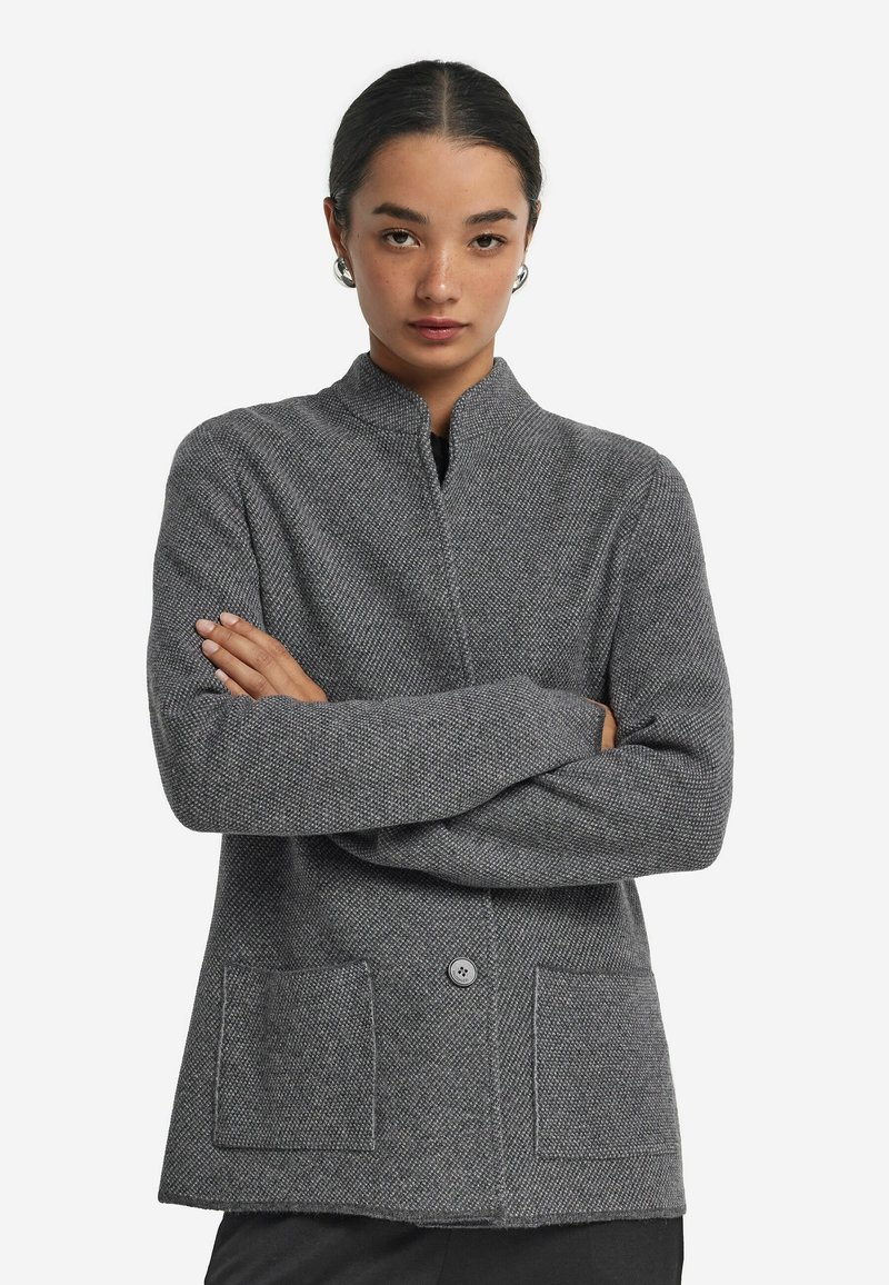 Szary, fakturowany żakiet z kołnierzykiem mandaryńskim, zapięciem na guziki z przodu i dwoma kieszeniami naszytymi. Wykonany z tkaniny plecionej o subtelnym wzorze.