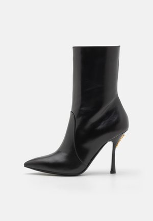 Czarne skórzane botki za kostkę z ostrym czubkiem, gładką teksturą i wysokim obcasem w kształcie stiletto. Posiadają rozcięcie z przodu oraz akcenty w złotym kolorze.