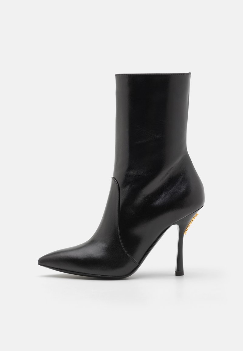 Cizmă scurtă din piele neagră cu vârf ascuțit, textură netedă și toc înalt stiletto. Prezintă o fanta în față și accente din metal aurit.