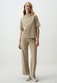 Completo beige a coste composto da un top a maniche corte con colletto alto e pantaloni a gamba larga, abbinato a sneakers chiare.