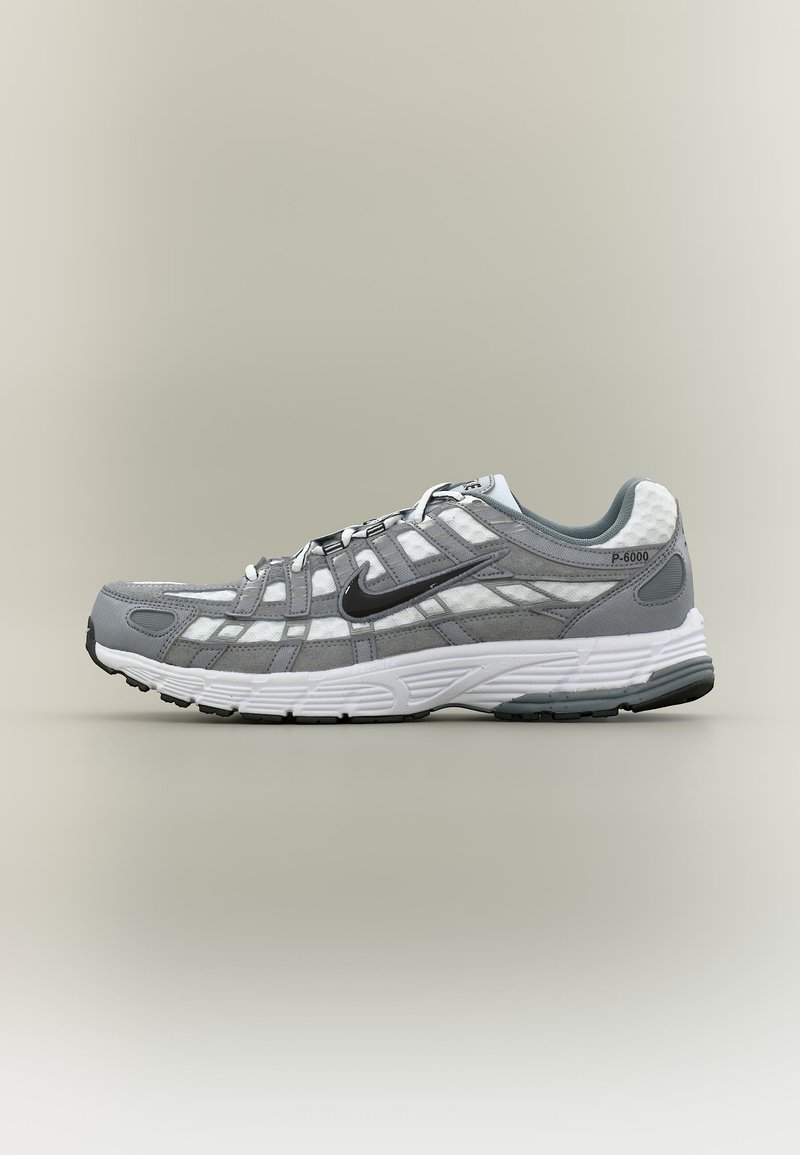 Γκρι και λευκό αθλητικό παπούτσι Nike P-6000 με μαύρο σήμα swoosh, επάνω μέρος από δίχτυ και σουέντ, και λευκή μαξιλαρωμένη σόλα, εμφανιζόμενο από το πλάι.