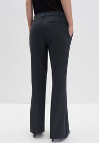 Pantalons ajustés gris foncé avec une taille cintrée, un design à jambes évasées, des détails de poches arrière et une texture lisse. Portés avec un haut rentré.