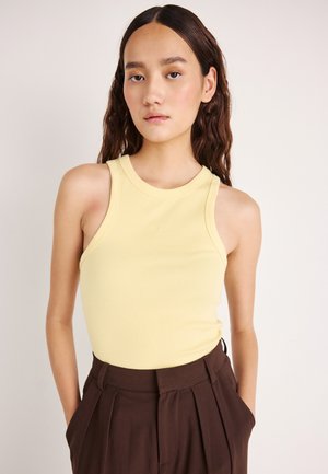 Canotta gialla a coste con scollo tondo e ampi spacchi per le braccia, abbinata a pantaloni marroni a vita alta. Tessuto liscio, stile aderente.