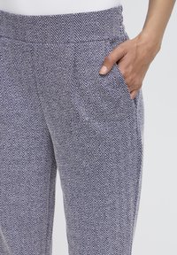 Nohavice s herringbone vzorom v námorníckej modrej a bielej farbe, s elastickým pásom a bočnými vreckami, vyrobené z mäkkej látky.
