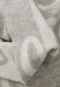 Blødt, foldet uldstof med et textureret grå- og hvidt cirkulært mønster, der viser nærbilleder af fibre og væv.