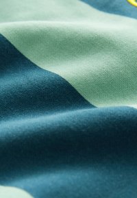 Bavlněná tkanina s zelenými a tyrkysovými pruhy, s jemnou texturou a mírným leskem, vykazující hladký, tkaný vzhled.