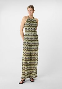 Green and patterned jumpsuit with a halter neck design, featuring zigzag stripes in black, white, and brown tones. Wide-leg silhouette.