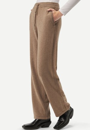 Braune Strickhose mit Kordelzug in der Taille, Seitentaschen und entspannter Passform. Kombiniert mit schwarzen Stiefeletten mit Absatz, die eine glatte Textur zeigen.