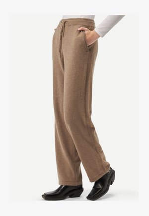 Pantalon en tricot brun avec taille à cordon, poches latérales et coupe décontractée. Associé à des bottes à talons noires, présentant une texture lisse.