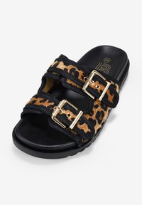 Sandalias deslizantes de print de leopardo con correas negras, hebillas doradas y una suela acolchada negra. Material texturizado similar a pelo en las correas.