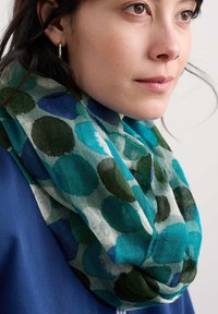 Sciarpa multicolore con motivi circolari blu e verdi su uno sfondo chiaro, realizzata in materiale leggero e trasparente, appoggiata attorno al collo.