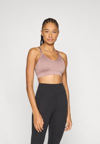 Lyse lilla sports-bh med sømløst design, tynde stropper og justerbar hardware. Kombineret med højtaljede sorte leggings. Glat tekstur.