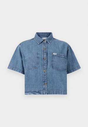 Camisa de mezclilla cortada en azul claro con mangas cortas, frente abotonado, dos bolsillos en el pecho y una pequeña etiqueta de la marca en el bolsillo izquierdo.