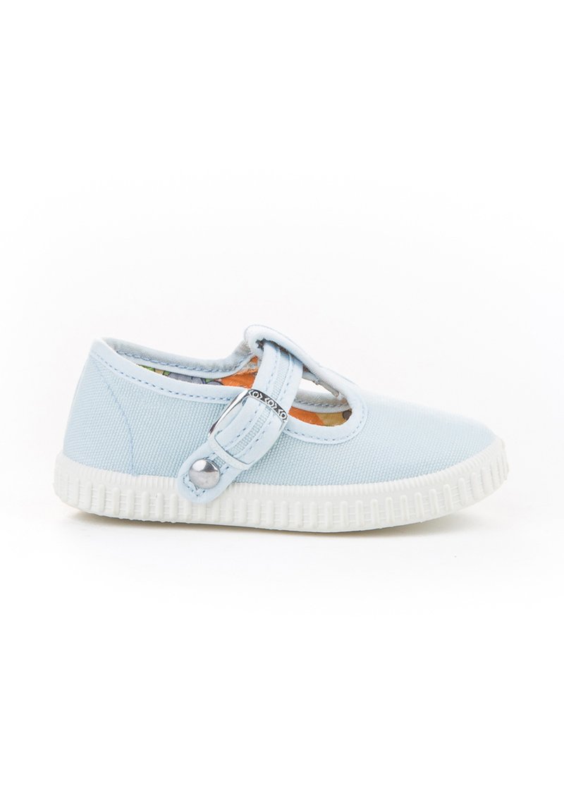 Zapato de lona azul claro con punta redondeada, correa cruzando el empeine y suela de goma blanca. Presenta un acento decorativo de botón en la correa.