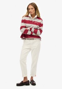 Polo a maniche lunghe a righe rosse e grigie con colletto bianco, abbinata a jeans bianchi e mocassini scuri. Polsini dei pantaloni arrotolati.