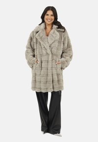 Płaszcz z futra syntetycznego w jasnoszarym kolorze, z teksturowanym wzorem w paski, w wersji oversize, z szerokim kołnierzem i bocznymi kieszeniami. Zestawiony z czarnymi spodniami.